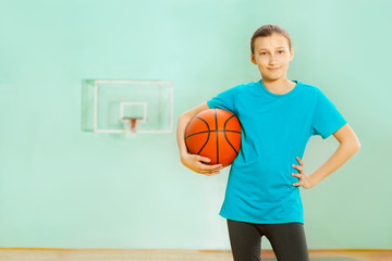 Naklejka premium Happy girl standing with basket ball in gym