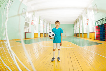 Fototapeta na wymiar Boy standing with soccer ball in school gymnasium