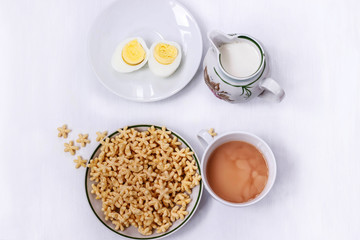 a healthy Breakfast of corn flakes, eggs, milk and tea on a white table