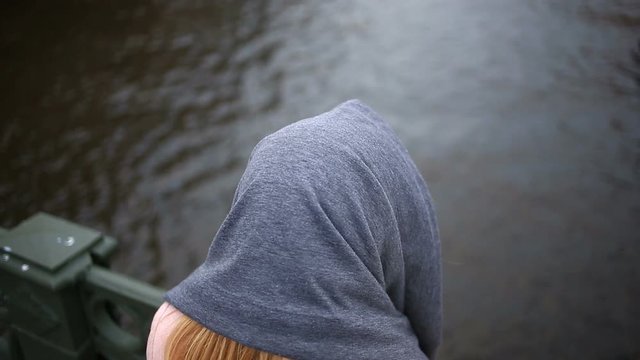A woman in a coat stands on a bridge and looks down at the black water. She wants to commit suicide