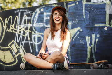 Fototapeta na wymiar Young female hangout at the skate park.She sitting on the ramp.