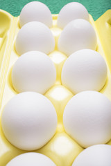 Ten white chicken eggs lie in a yellow tray, a vertical frame