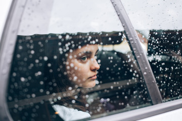 Close up of sad and offended girl sitting inside the car while it rains and storms outside, she...