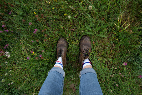 Top shot of hard brutal leather boots and legs wearing denim jeans, stand in middle of grass field full of flowers