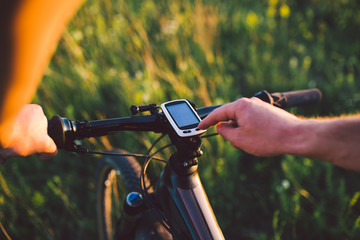 A young brunette guy on a mountain bike uses a cycling computer, a navigator in the field sunset of...