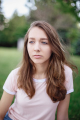 Fototapeta premium Portrait of young beautiful white Caucasian woman girl sitting on grass in park outside on summer day, toned with retro filters, film effect, candid lifestyle