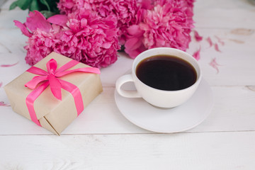 A cup of coffee, pink peonies pattern and gift box on wooden background