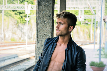 Attractive blond young man standing on railroad tracks, wearing white t-shirt, looking away