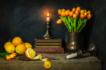 Classic still life with fresh oranges placed with beautiful orange tulip flowers,illuminated candle...