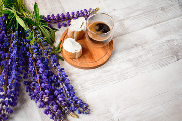 A Cup of coffee,note book , cracker, cookie, biscuit, lupins flowers on a wooden table.