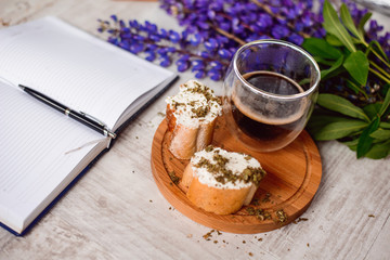 A Cup of coffee,note book , cracker, cookie, biscuit, lupins flowers on a wooden table.