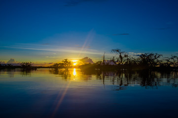 Fototapeta na wymiar Beautiful silhouetted against an orange sky at sunset over Laguna Grande in the Cuyabeno National Park, in Ecuador