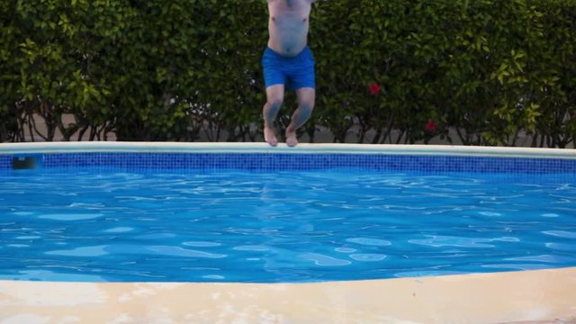Slow motion shot. Young Man jump into swimming pool at tropical island hotel. Teal and orange. Sunny day. Azur blue water.