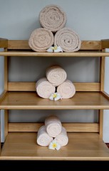 Rolls of beige towels on the shelves  Beige towels rolled and arranged on the shelves decorated with white plumeria flowers