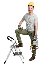 Smiling man in a grey shirt and green pants with a safety helmet standing in front of a white background holding a hammer and a lamp. Looking at camera.