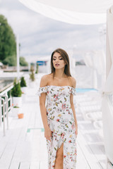 Portrait of a beautiful woman in a dress posing on a white wooden beach of summer.