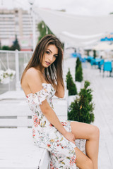 Portrait of a beautiful woman in a dress posing on a white wooden beach of summer.