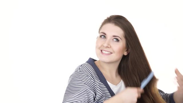 Woman wearing bath robe combing her healthy hair with blue comb. Young female with beauty straight long brown hairs -studio shot isolated on white background 4K ProRes HQ codec
