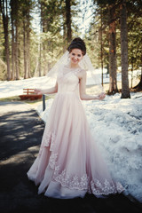 Fototapeta na wymiar Spring portrait of a bride, dressed in pink wedding dress in the snowy forest.