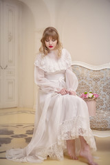 girl in white vintage dress sitting on the sofa with a bouquet of roses