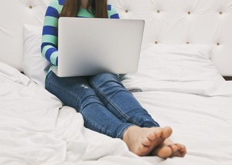The young woman is lying on the bed with a laptop