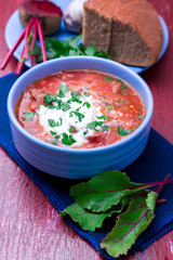 Ukrainian traditional borsch. Russian vegetarian red soup  in blue bowl on red wooden background.  Borscht, borshch with beet. Close up.