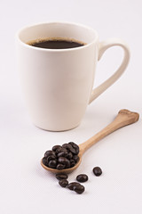 Coffee cup and beans on wooden spoon on white background.