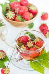 Glass cup of summer tea with fresh strawberry. Green leaves. Fresh mint. White wooden table. Shallow depth of field.