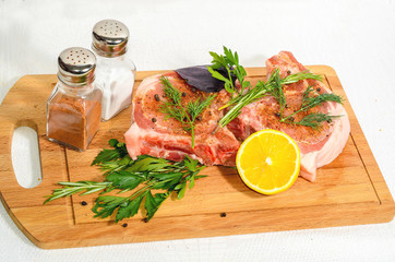Two appetizing pieces, pork entrecote on a wooden cutting board with salt shaker and pepper and rosemary and lemon