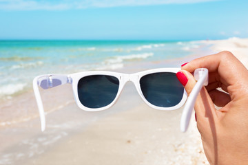 Sunglasses in hand on background of the beach
