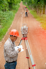 Surveyor or Engineer making measure by Theodolite with partner on the street in a field.