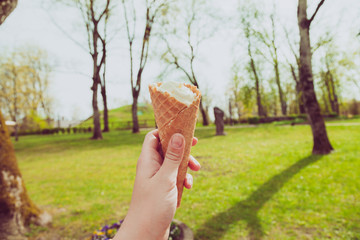 Hand holding ice cream in cone on warm summer day in park