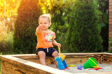 Happy little girl playing in a sandbox on the playground. Summertime children activities