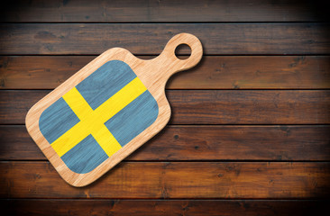 Concept of Swedish cuisine. Cutting board with a Sweden flag on a wooden background