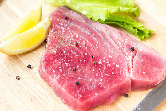 Fresh raw tuna fillet with black pepper corns, salt, lemon and olive oil on rustic background. Raw tuna steak on wooden cutboard, close up, selective focus, ingredients for cooking