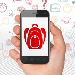 Education concept: Hand Holding Smartphone with Backpack on display