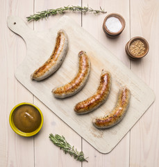 grilled sausages lying on vintage cutting board with rosemary, spices, curry sauce and meat fork on a rustic background top view