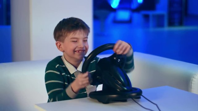 Happy excited little boy playing videogame with racing wheel