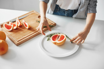 Close up of girl decorating plate with half of grapefruit and rosemary. Diet healthy food.