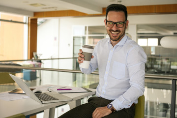 Business man in office having a break. Man with cup of coffee looking at camera.
