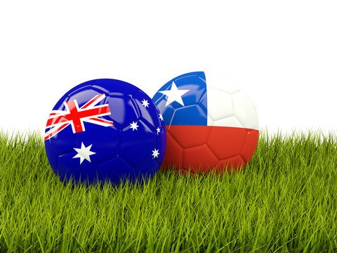 Two footballs with flags of Australia and Chile on green grass