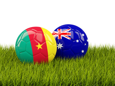 Two footballs with flags of Cameroon and Australia on green grass
