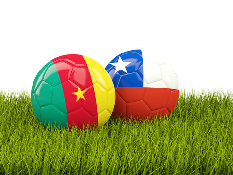 Two footballs with flags of Cameroon and Chile on green grass