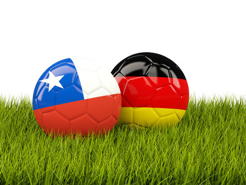 Two footballs with flags of Chile and Germany on green grass