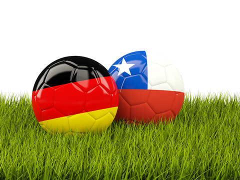 Two footballs with flags of Germany and Chile on green grass