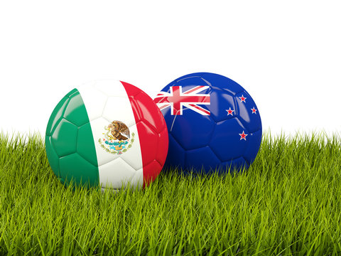 Two footballs with flags of Mexico and New Zealand on green grass