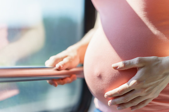 pretty tummy of pregnant european women close to train window while she traveling by rail way and holding handrail inside the carriage