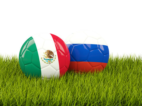 Two footballs with flags of Mexico and Russia on green grass