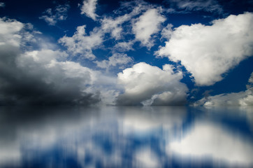 Naklejka na ściany i meble Blue sky. Dramatic clouds over sea. Blurred reflection of sky in water