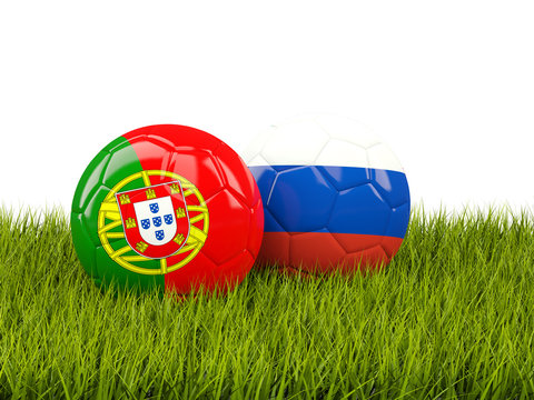 Two footballs with flags of Portugal and Russia on green grass